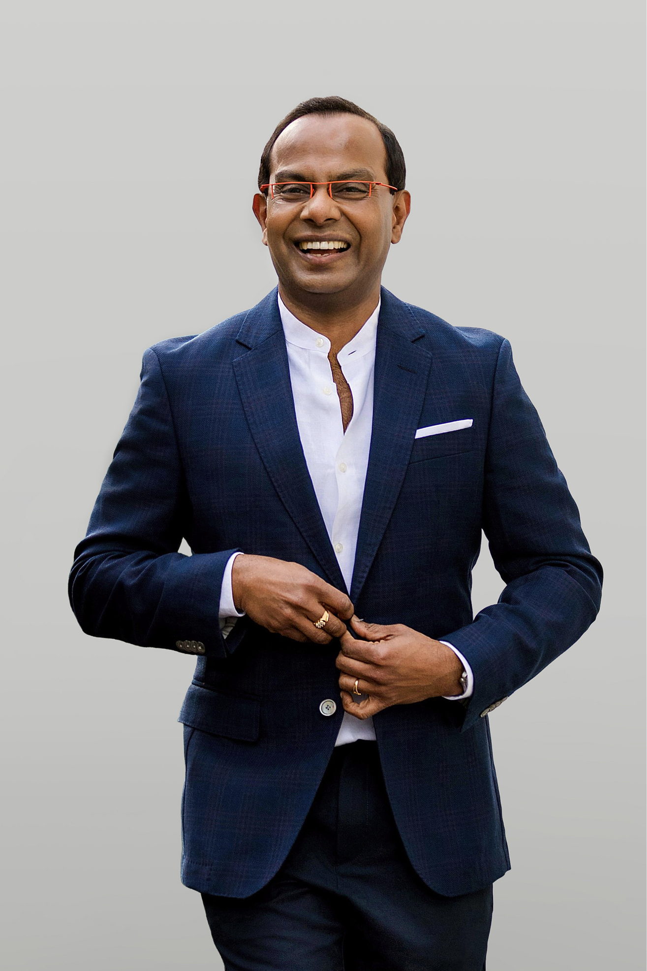 Smiling man in a navy suit with white shirt, clasping his hands in front against a gray backdrop