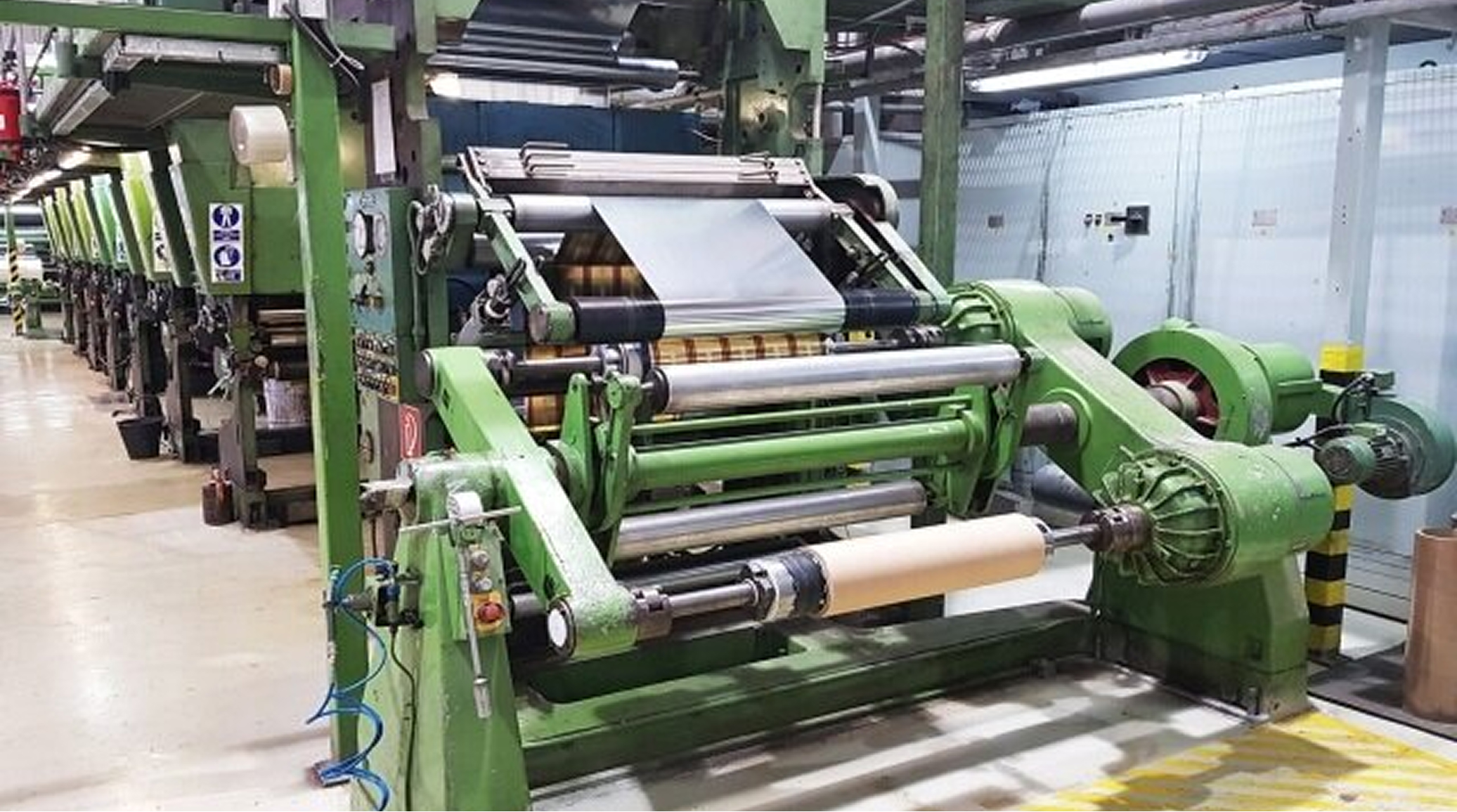 Industrial textile loom with a green framework and multiple rollers in a factory setting